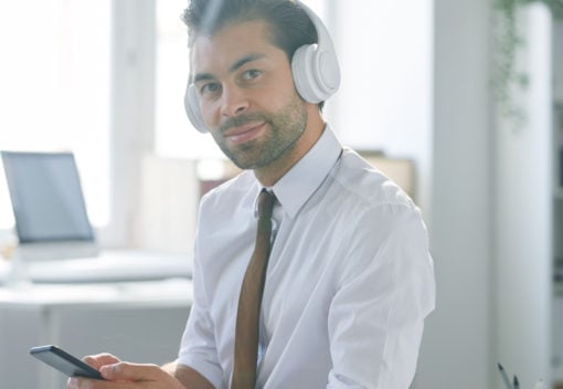 Confident young office worker in headphones using smartphone